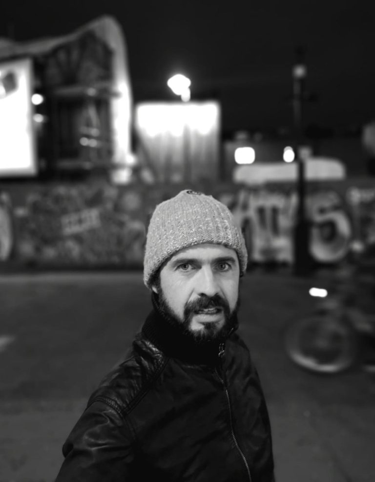 Neil Atkinson, the photographer, wearing a beanie, standing in an urban setting at night.